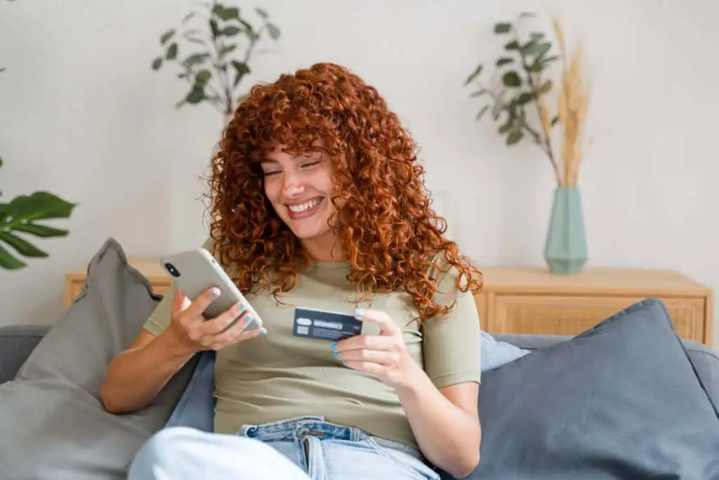 Happy woman using smartphone for online shopping on sofa at home