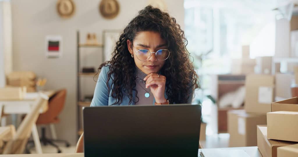 Boxes, thinking and woman with a laptop, ecommerce and connection with website information, email or planning. Person, entrepreneur and employee with pc, brainstorming and business owner with startup