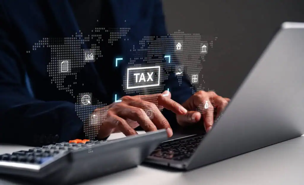 A person using a laptop with a digital tax interface displayed, surrounded by a global map and financial icons, emphasizing modern financial management.