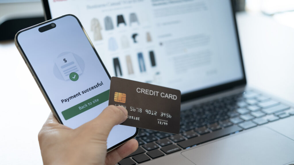 Holding a credit card with a phone screen saying Payment successful in front of a shopping website, symbolizing smooth spending in the digital era